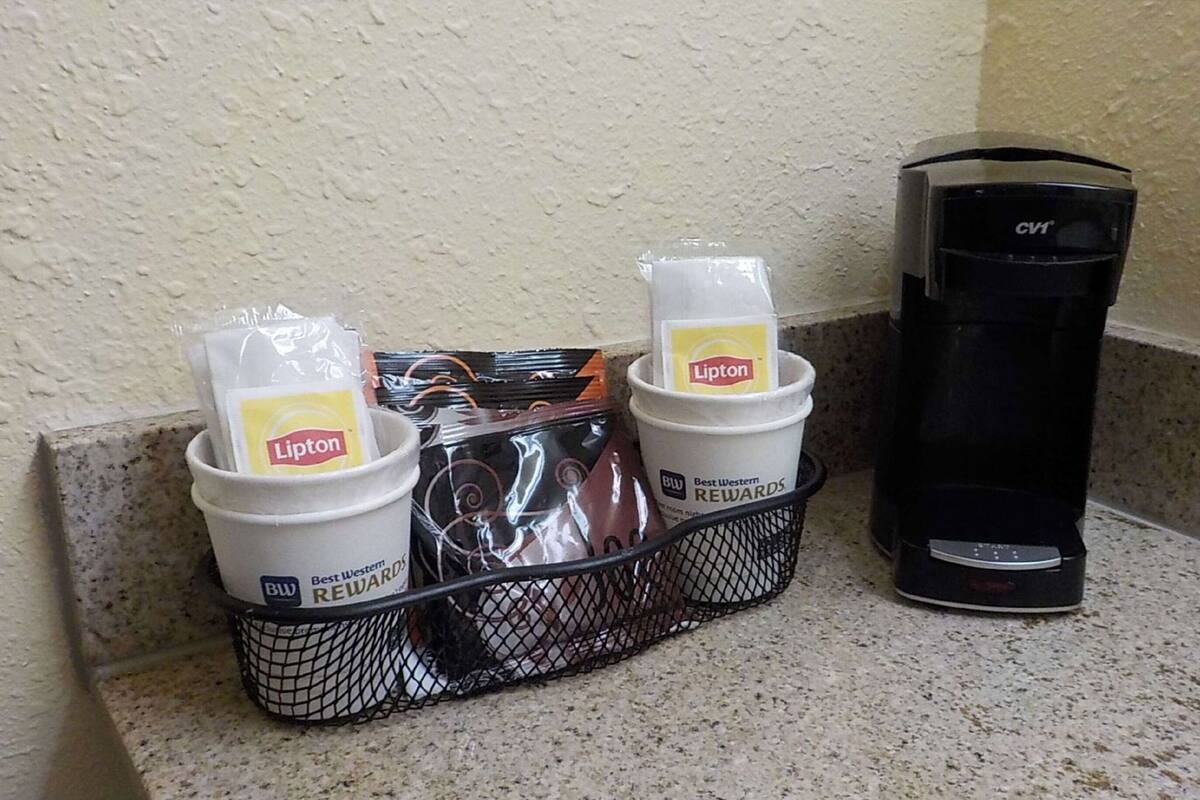 En kaffemaskine, en Lipton-te-dispenser og en kurv med Lipton-tebreve på en bordplade.