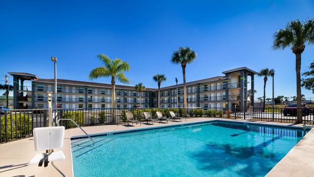 Un hotel con piscina, palmeras y un cielo azul despejado.