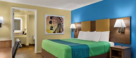 Habitación de hotel con cama, mesitas de noche, un escritorio y una silla. Se observa un cuadro en la pared y una puerta que da a otra habitación.