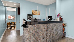 Un área de recepción con un mostrador de baldosas, una máquina de café, un monitor de computadora y un jarrón con flores.