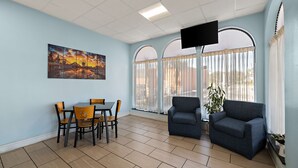 Una habitación con mesa de comedor y sillas, dos sofás, un televisor de pantalla plana y ventanas amplias con cortinas.