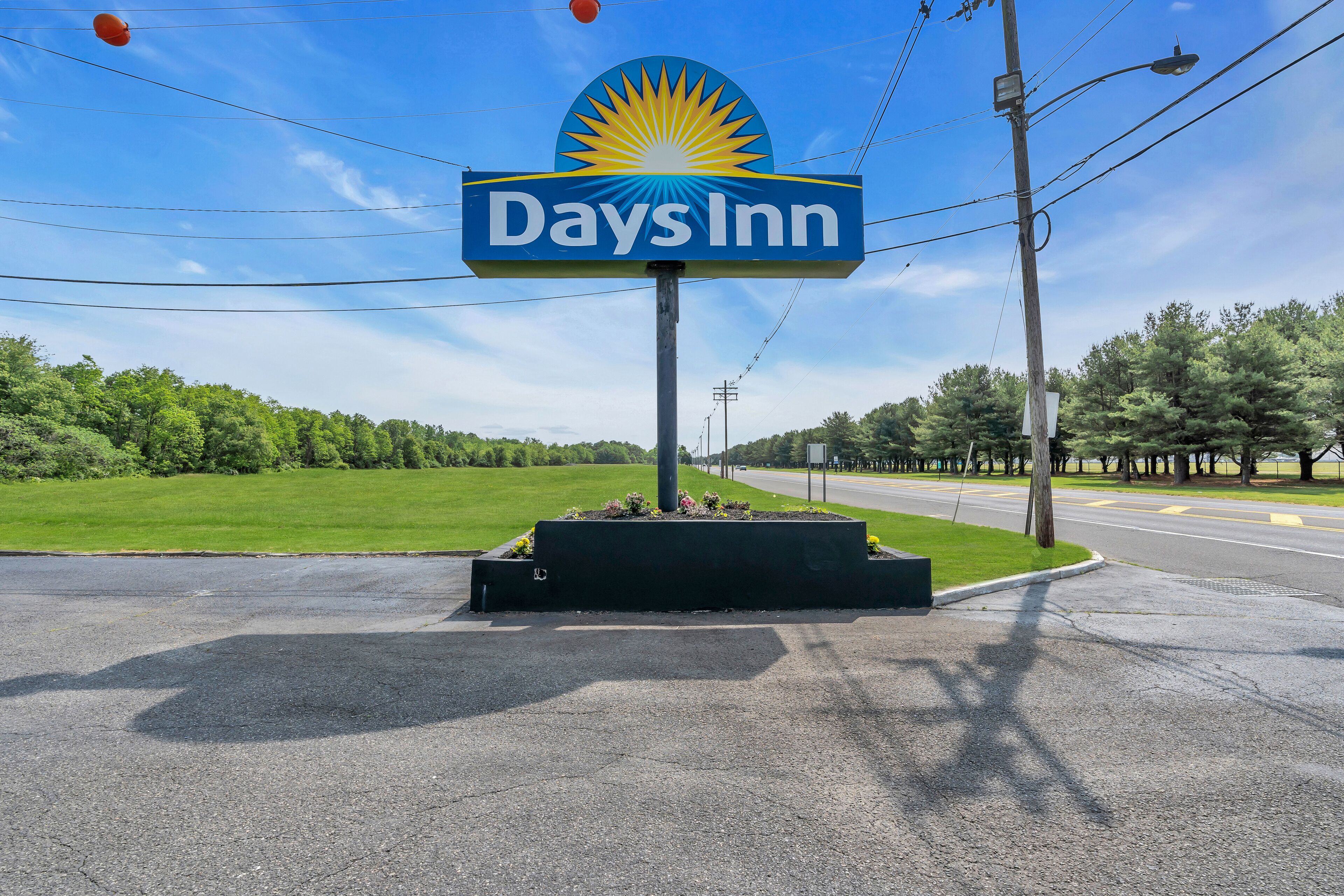 A Days Inn sign with a sun emblem, surrounded by greenery and a road.