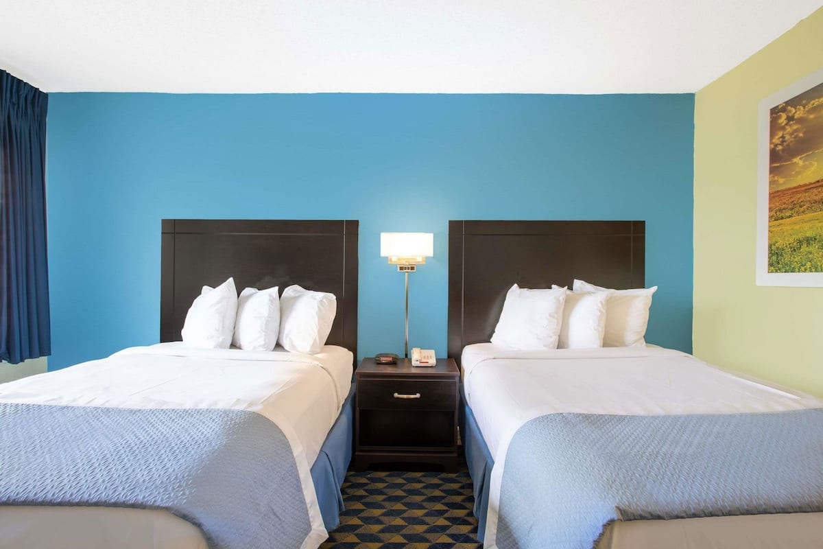 Una habitación de hotel con dos camas, una mesita de noche con lámpara y un mostrador de recepción.