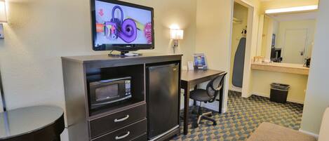 Habitación de hotel con televisión de pantalla plana, microondas, escritorio, silla, mesita y alfombra estampada.