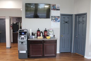 Un espace cuisine équipé d’un distributeur automatique de billets, d’une machine à café et d’un tableau d’affichage.
