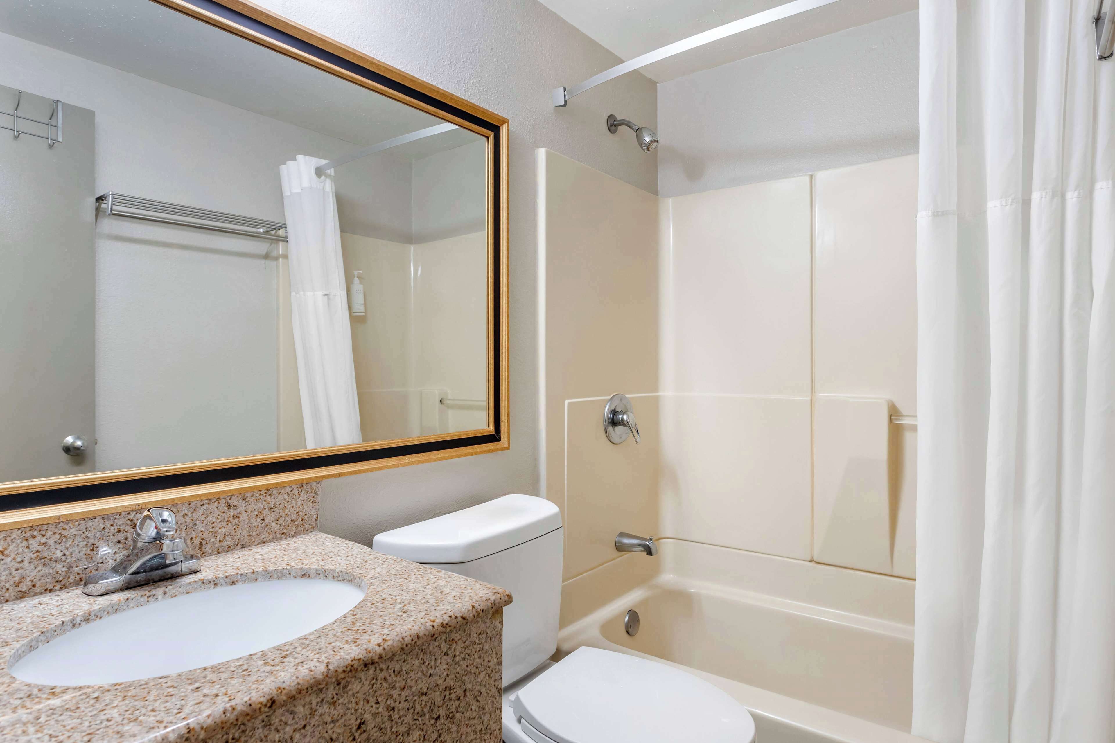 A bathroom with a granite countertop sink, a toilet, a bathtub, and a mirror with a gold frame.