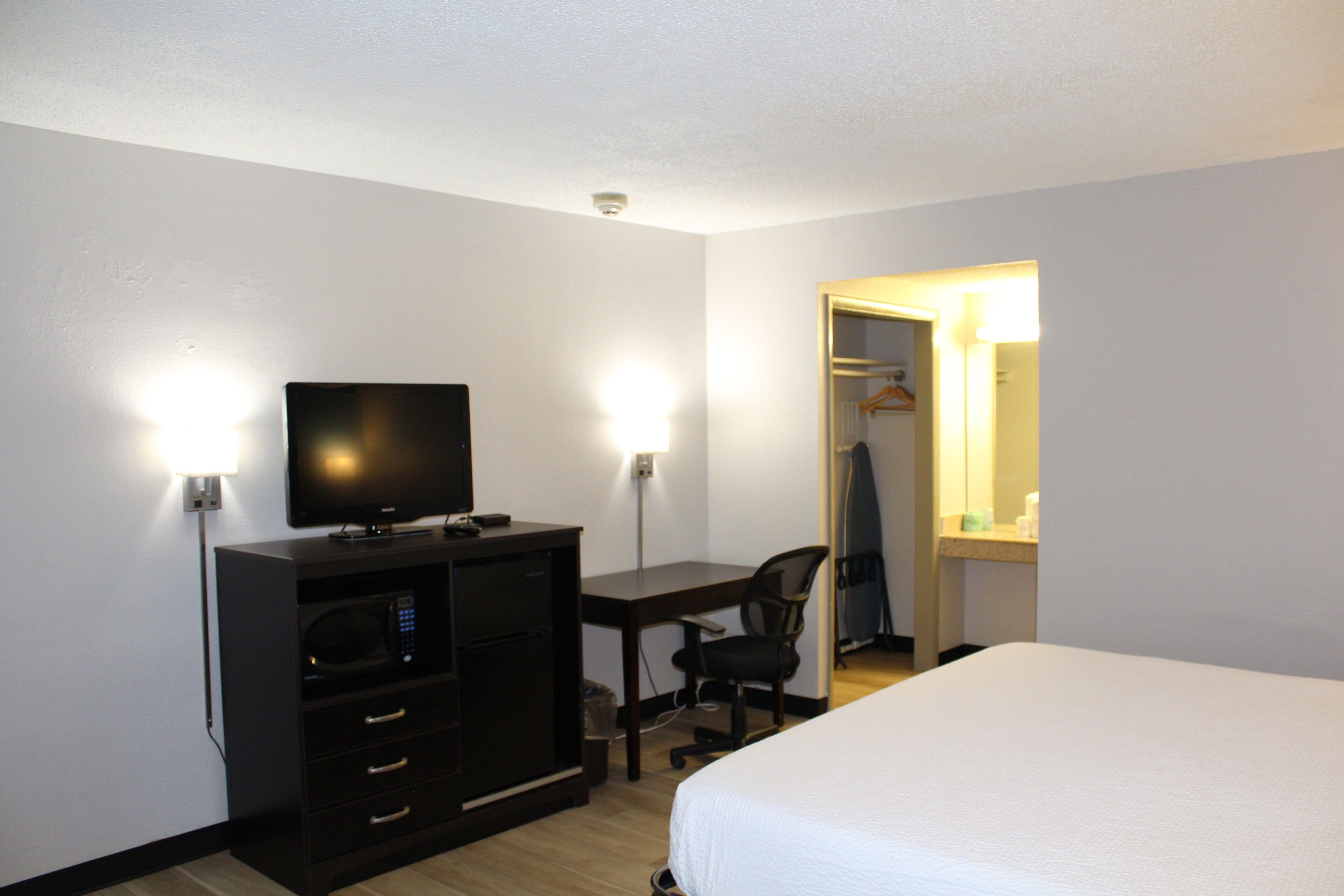 Una habitación de hotel con una cama, un escritorio con computadora, televisor y armario.