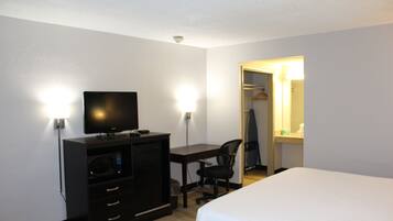 Una habitación de hotel con una cama, un escritorio con computadora, televisor y armario.