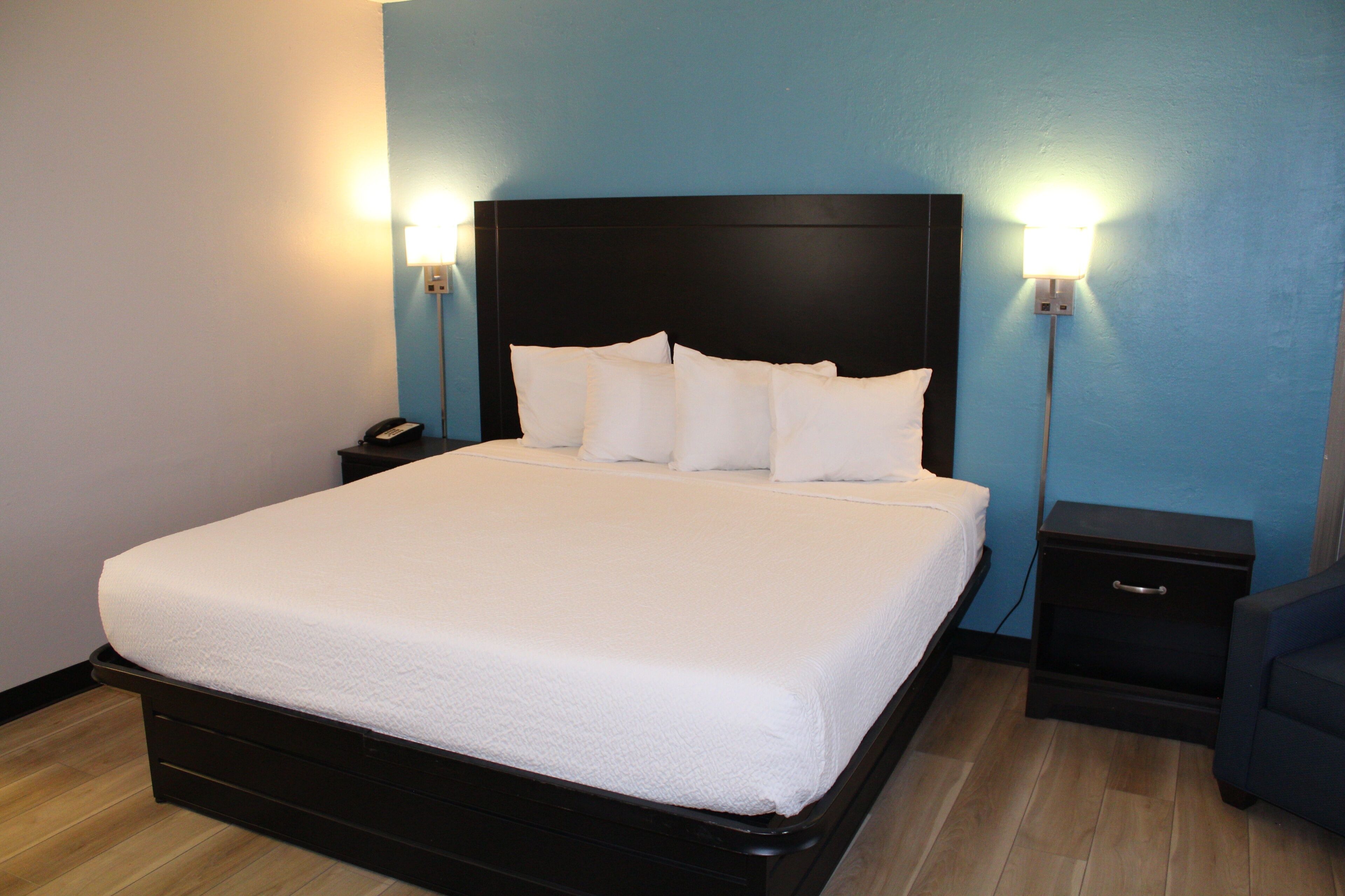 A neatly made bed with a black headboard, two bedside tables with lamps, and a blue wall.