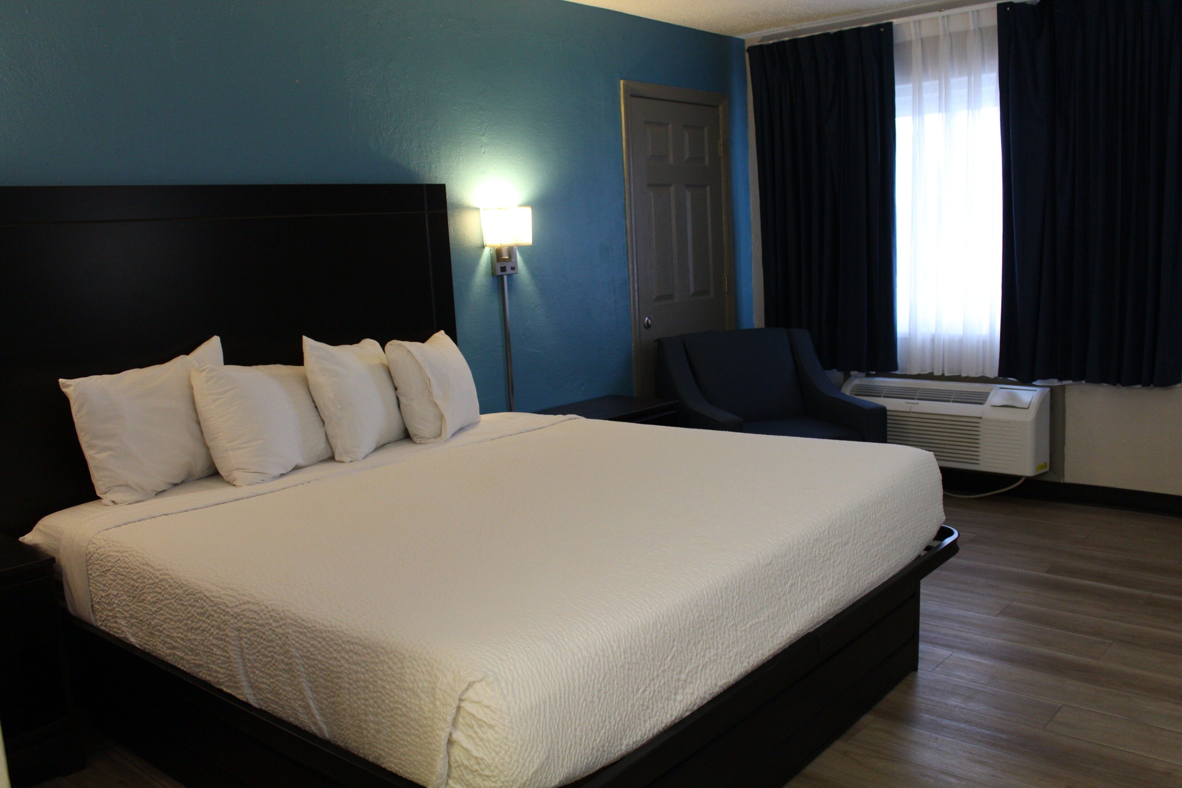 Ein Hotelzimmer mit einem großen Bett, einem Nachttisch, einem Schreibtisch, einem Sessel und einem Fenster mit Vorhängen.