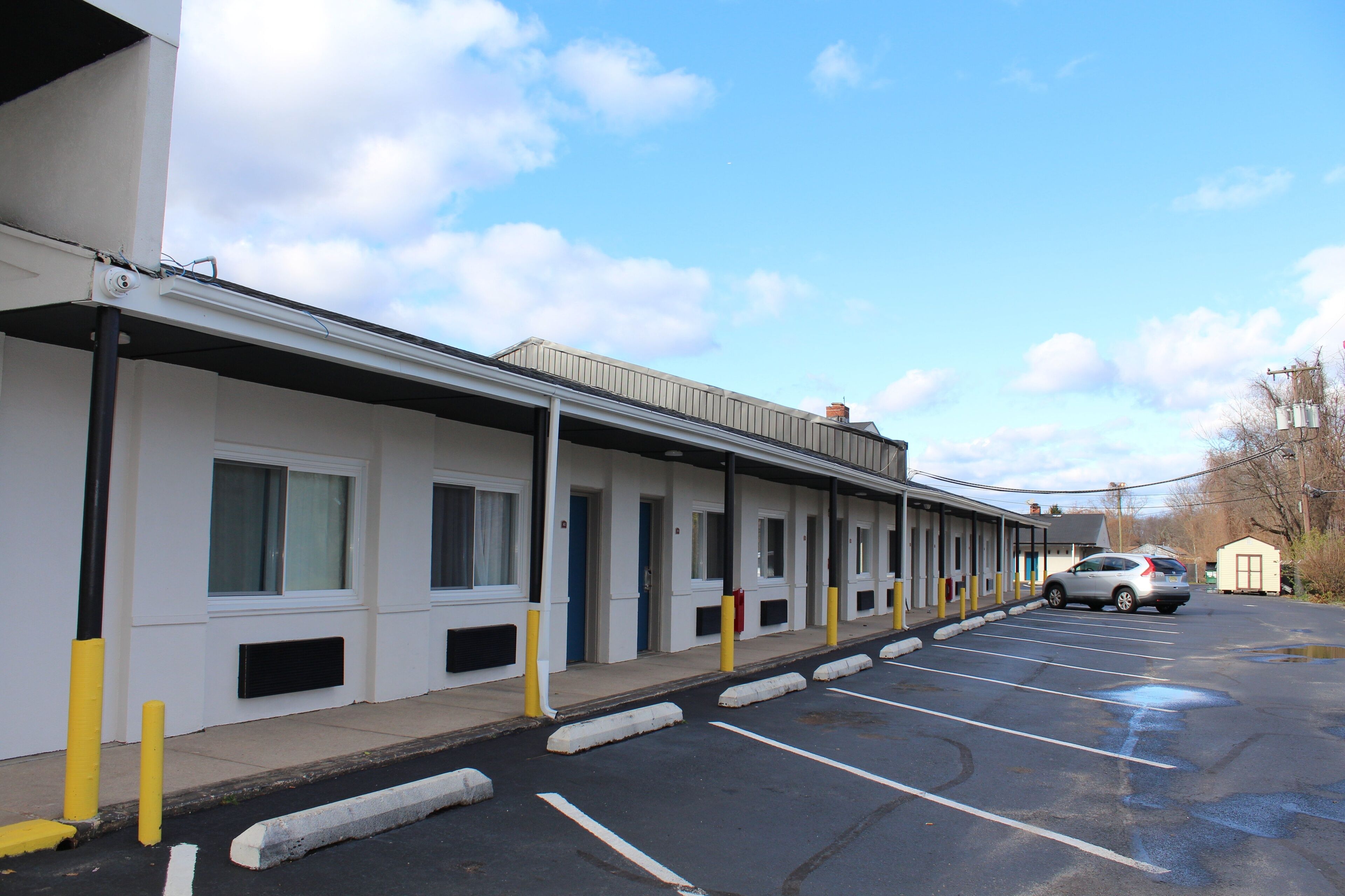 A motel with a row of rooms, a parking lot, and a clear sky.