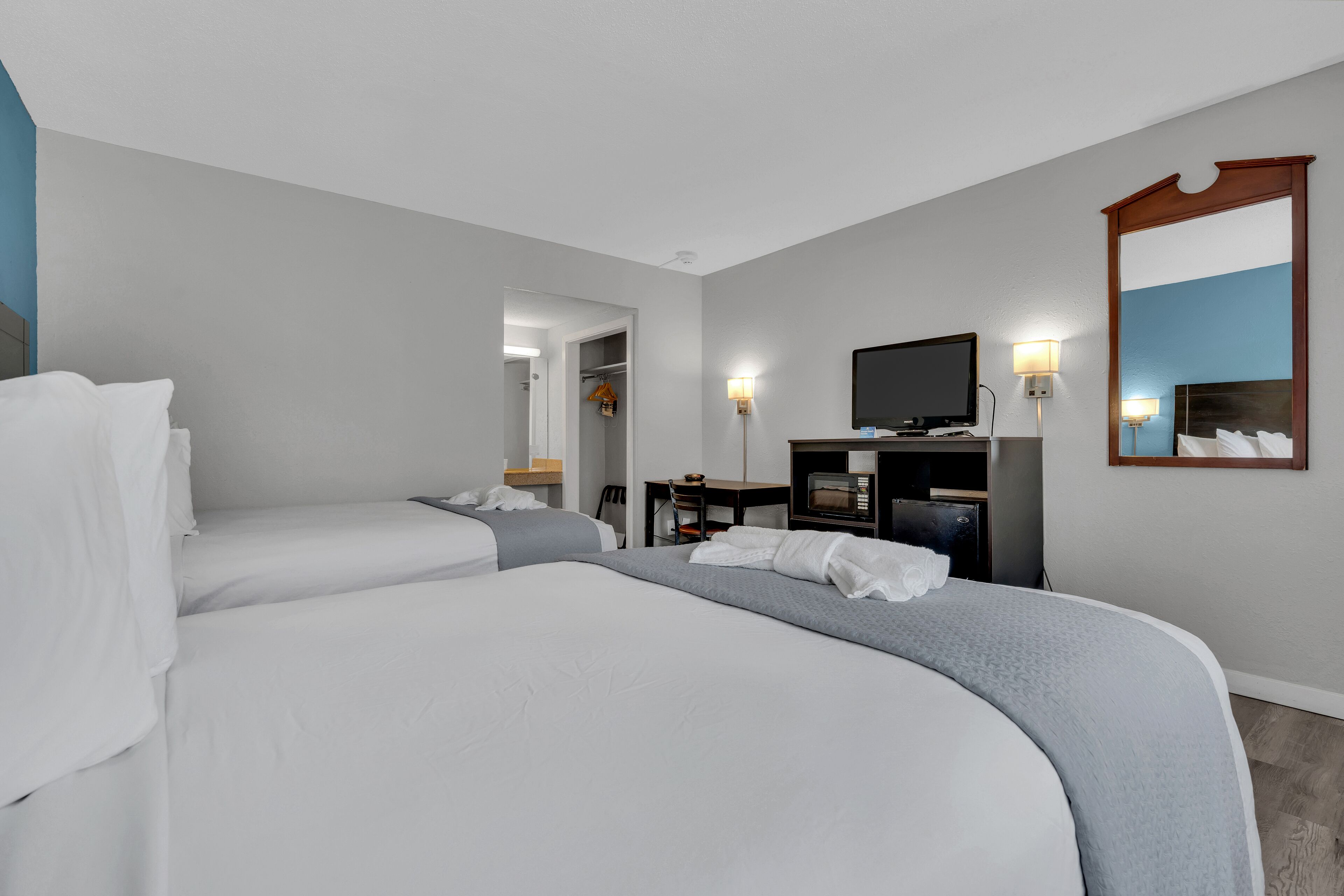 Ett hotellrum med två sängar, ett skrivbord med en stol, en tv och en spegel på väggen.