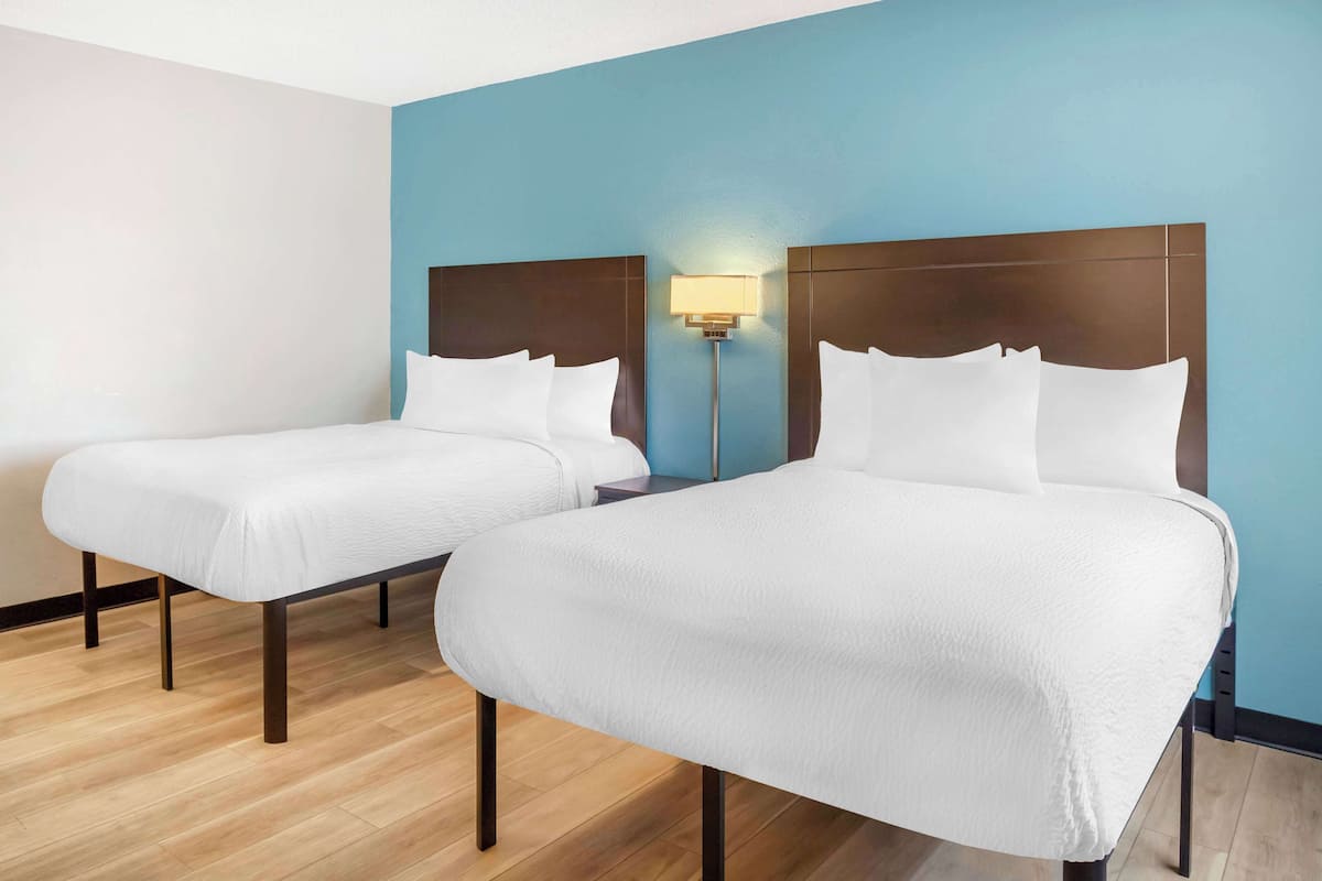 Dos camas individuales con sábanas blancas en una habitación con suelo de madera clara y paredes azules.