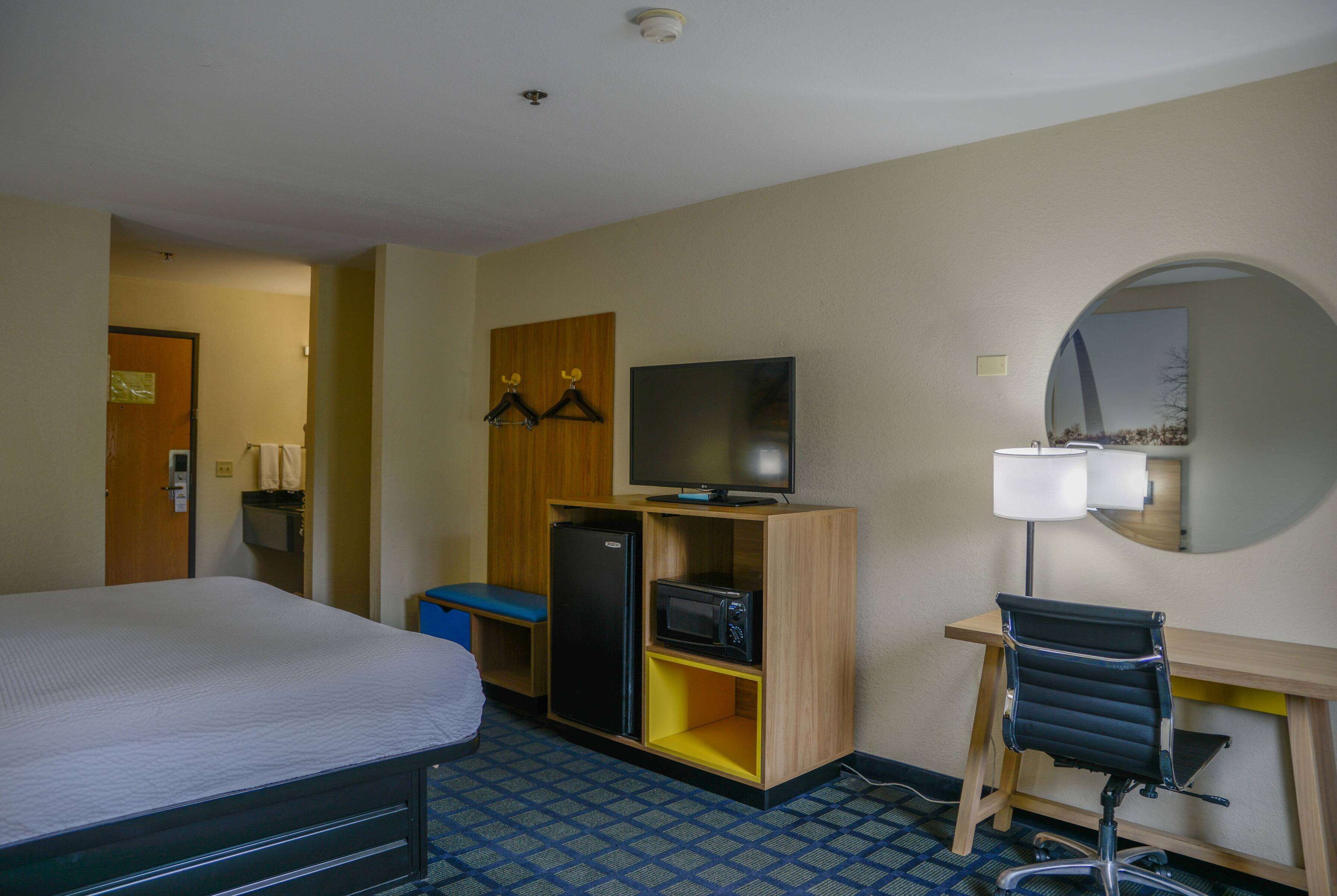 Habitación de hotel con cama, escritorio y silla, televisor, refrigerador y microondas.