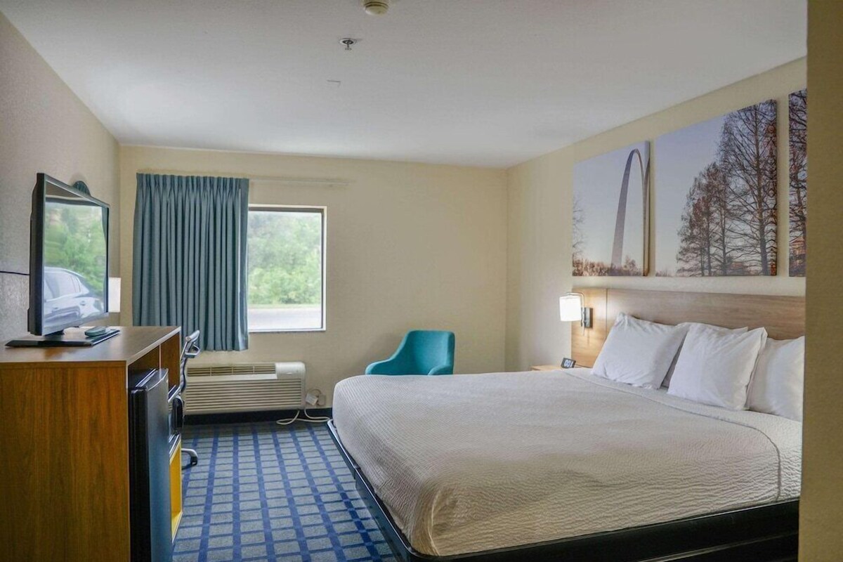 A hotel room with a bed, a desk, a chair, a television, and a window with curtains.