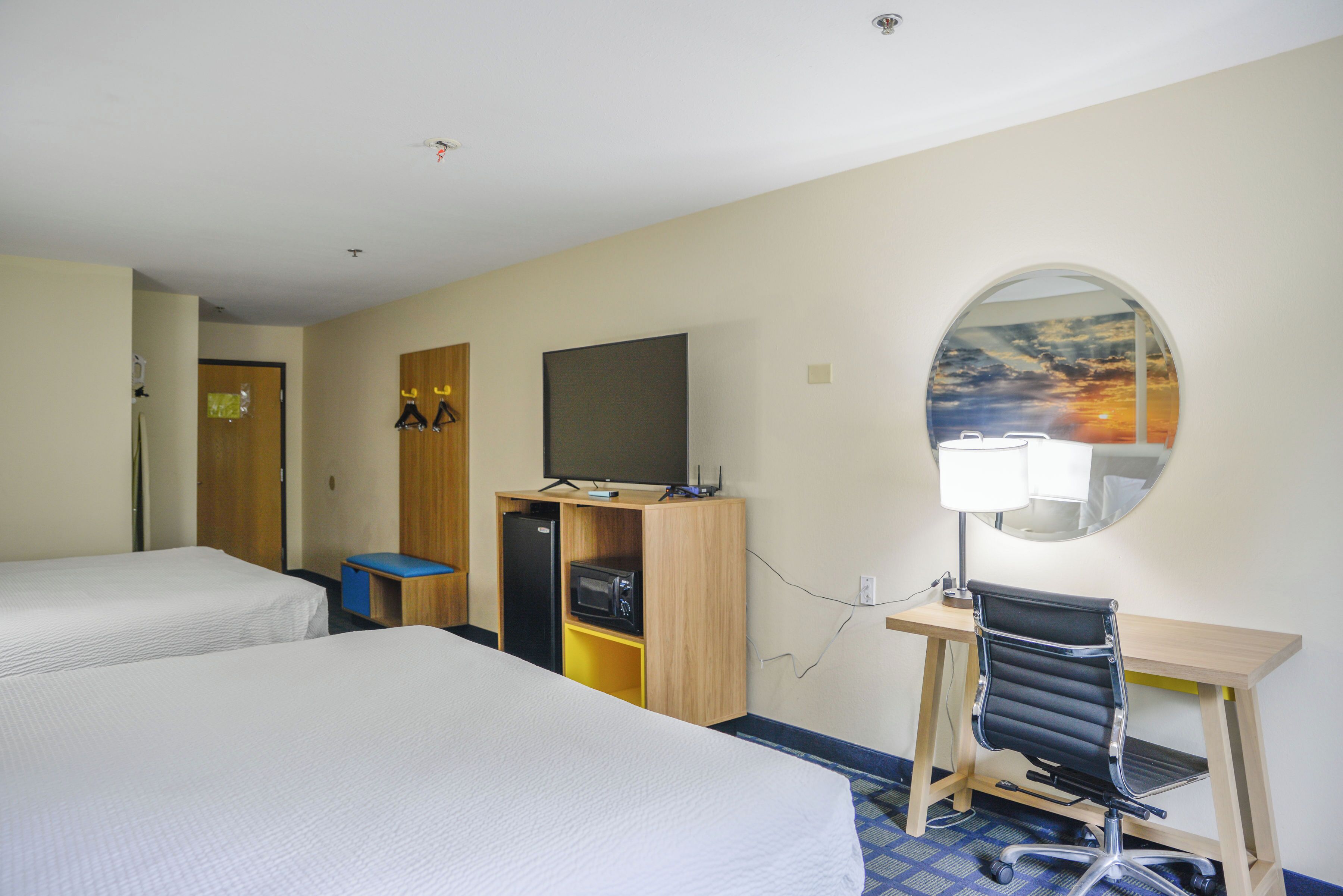 Ett hotellrum med två sängar, ett skrivbord med en stol, en tv, en mikrovågsugn och en spegel med utsikt över solnedgången.