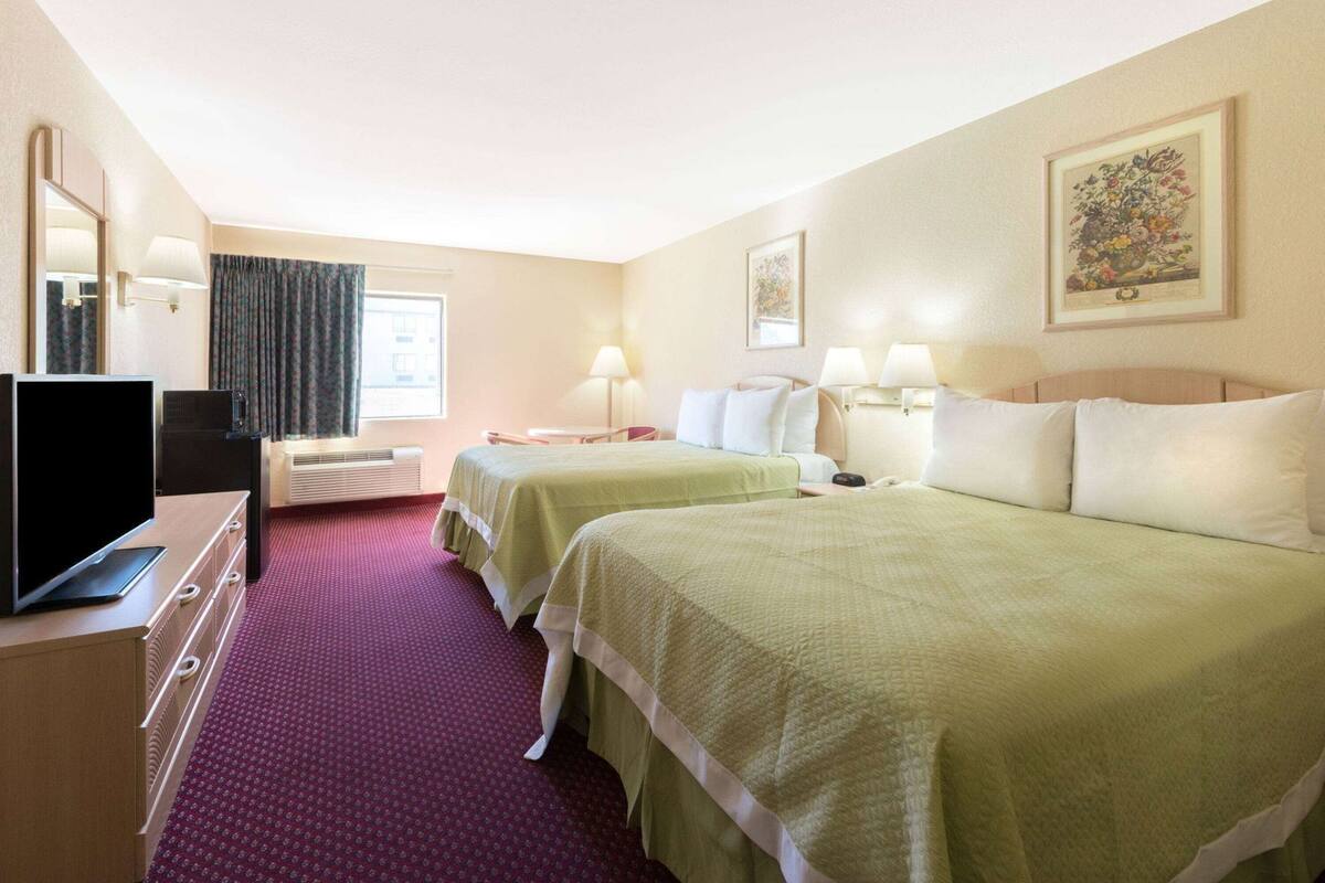 A hotel room with two beds, a television, a desk, and a window with curtains.