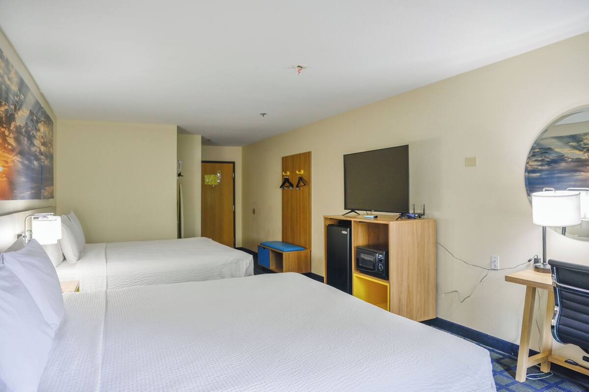 A hotel room with two beds, a desk, a television, and a small refrigerator.