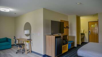 A hotel room with a bed, a desk with a computer, a refrigerator, a microwave, and a small bathroom.