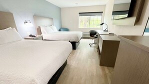 Ein Hotelzimmer mit zwei Betten, einem Schreibtisch, einem Stuhl, einer Schreibtischlampe und einem großen Fenster.