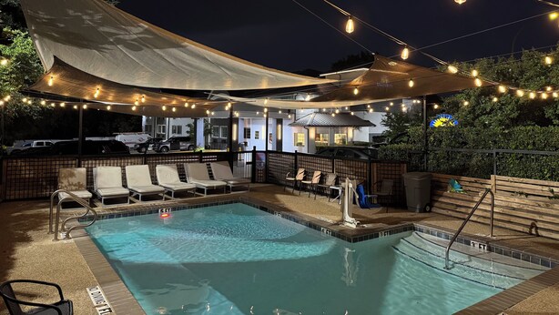 Ein Poolbereich mit Liegestühlen, einem Pool mit Tiefenmarkierungen und Lichterketten.