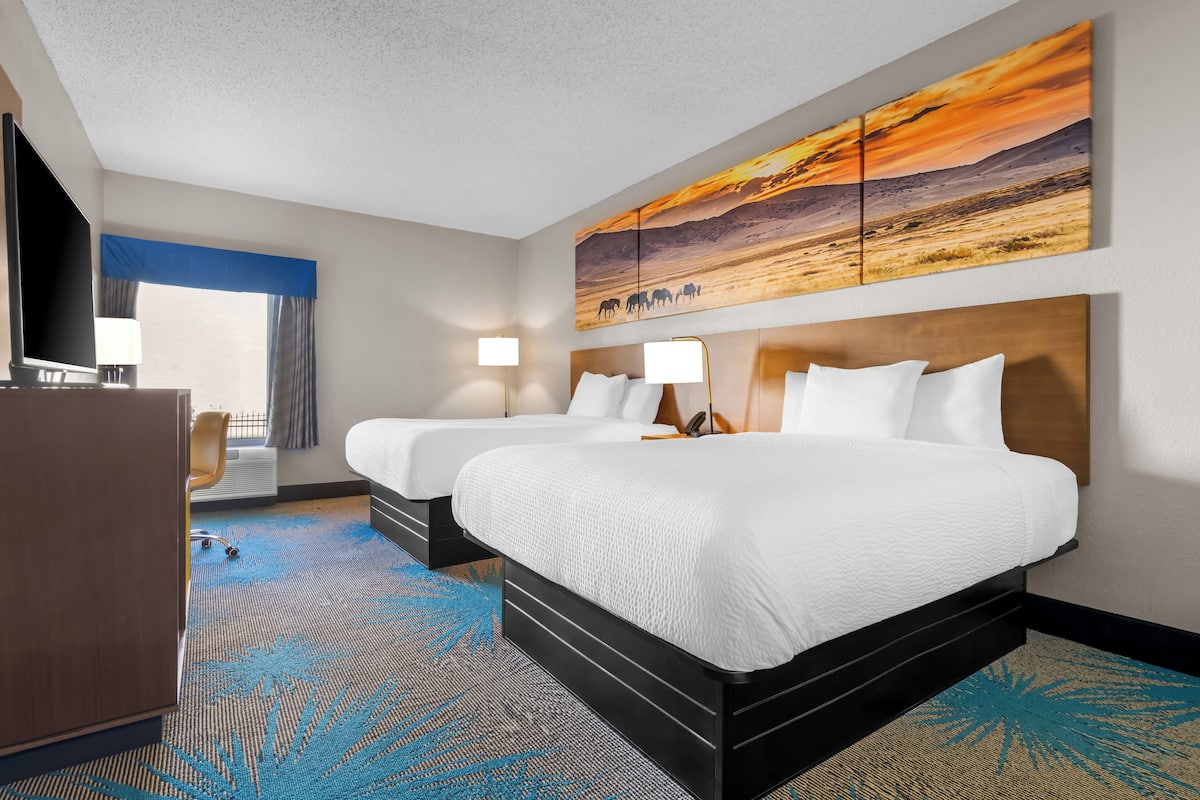 A hotel room with two beds, a desk, and a large painting of a sunset.