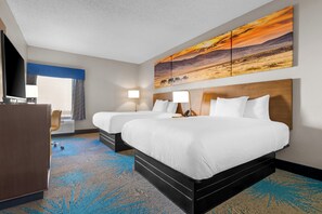 A hotel room with two beds, a desk, and a large painting of a sunset.