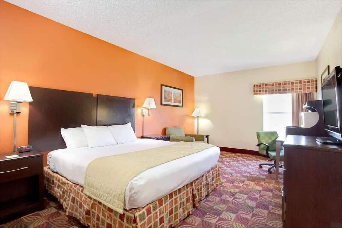 A hotel room with a bed, two bedside tables with lamps, a desk with a television, and a chair.