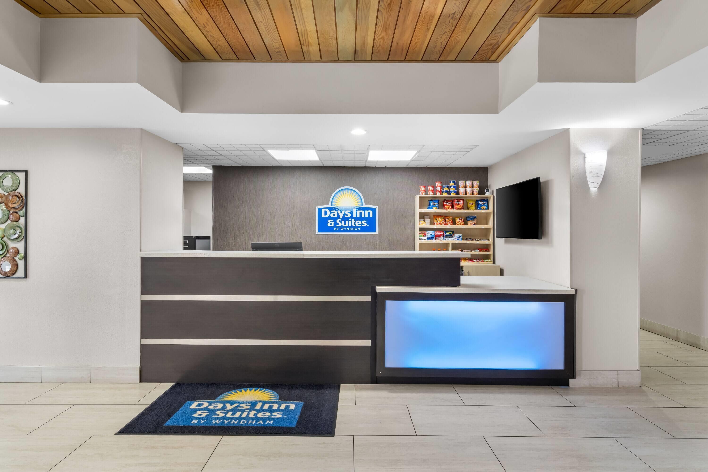 A reception area with a Days Inn & Suites sign, a reception desk, a digital display, and a shelf with snacks.