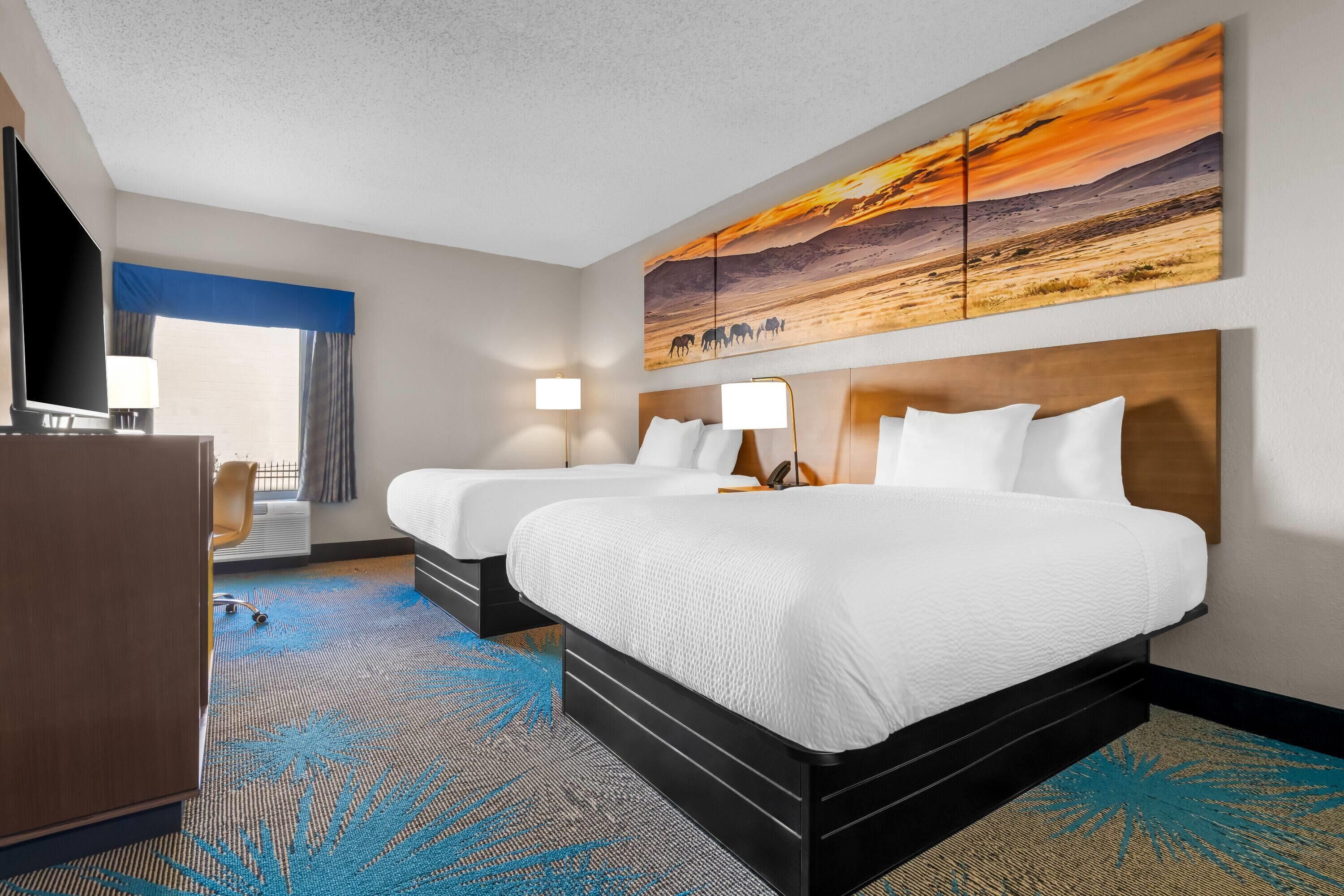 A hotel room with two beds, a desk, and a large wall painting.