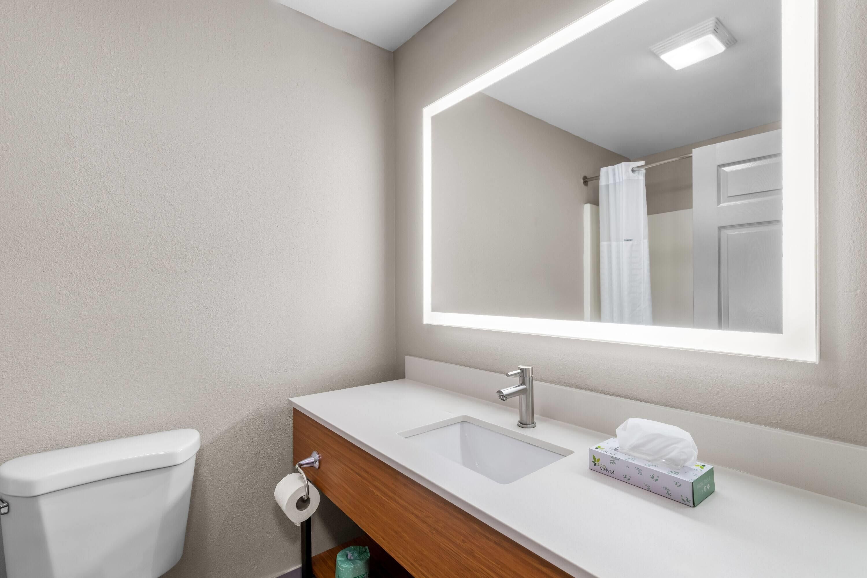 Un baño con lavamanos blanco, espejo y retrete.