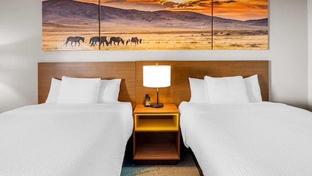 A hotel room with two beds, a wooden headboard, a nightstand with a lamp, and a large landscape painting above the beds. - Days Inn & Suites by Wyndham Ridgeland (Ridgeland)