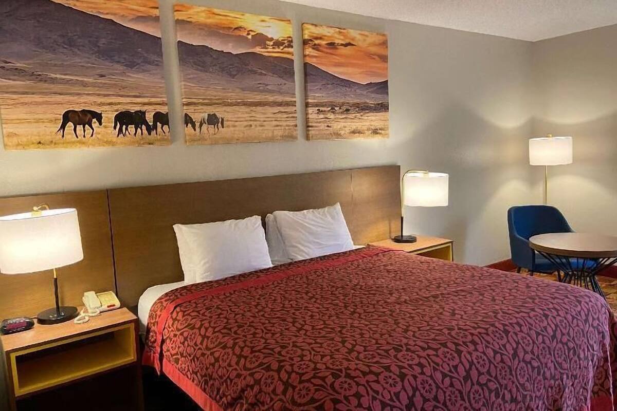 A hotel room with a large bed, two bedside tables with lamps, a chair, and a wall-mounted painting of a desert scene.