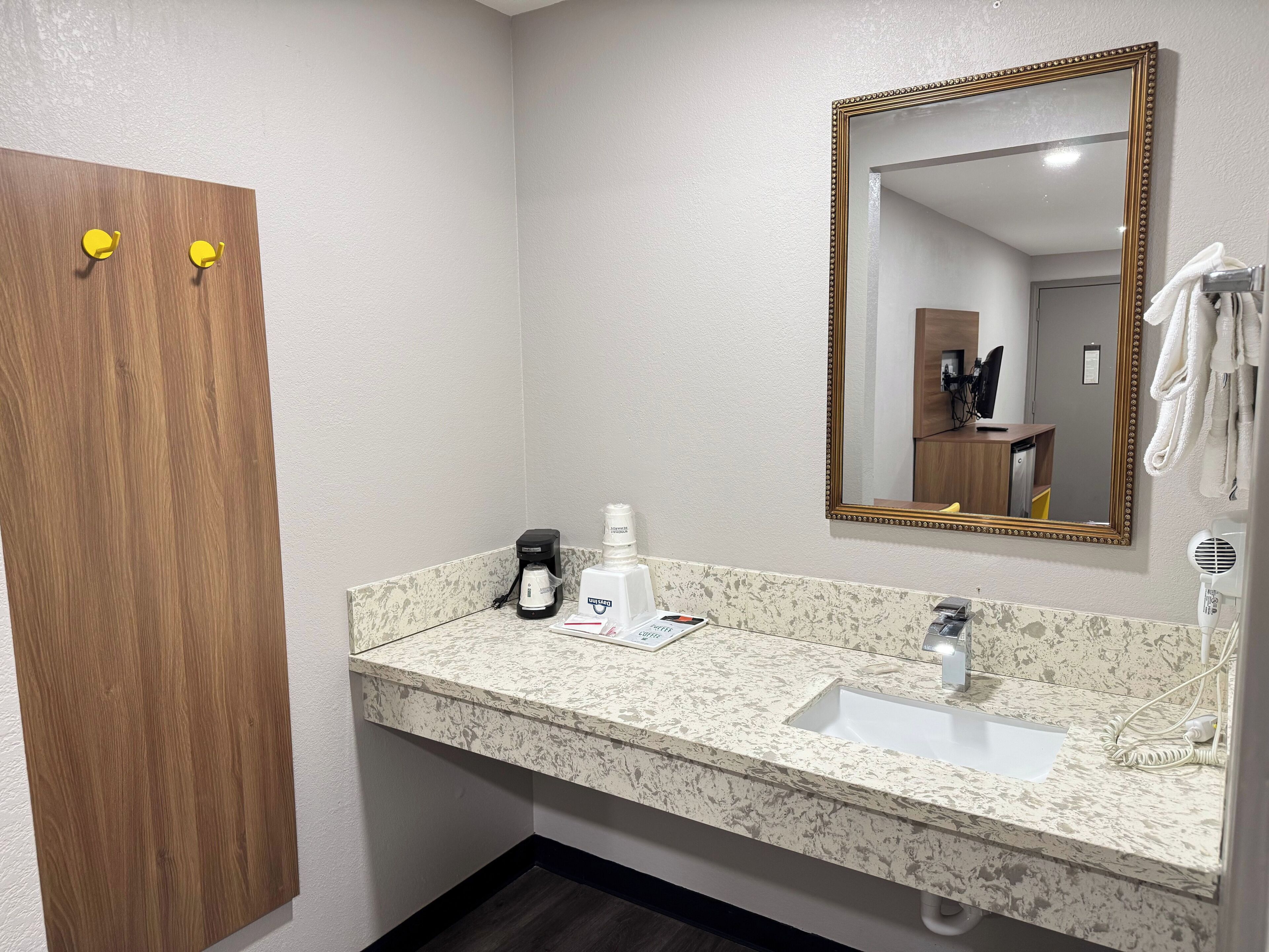 A bathroom with a wooden door, a sink with a marble countertop, a mirror with a gold frame, and a towel rack.