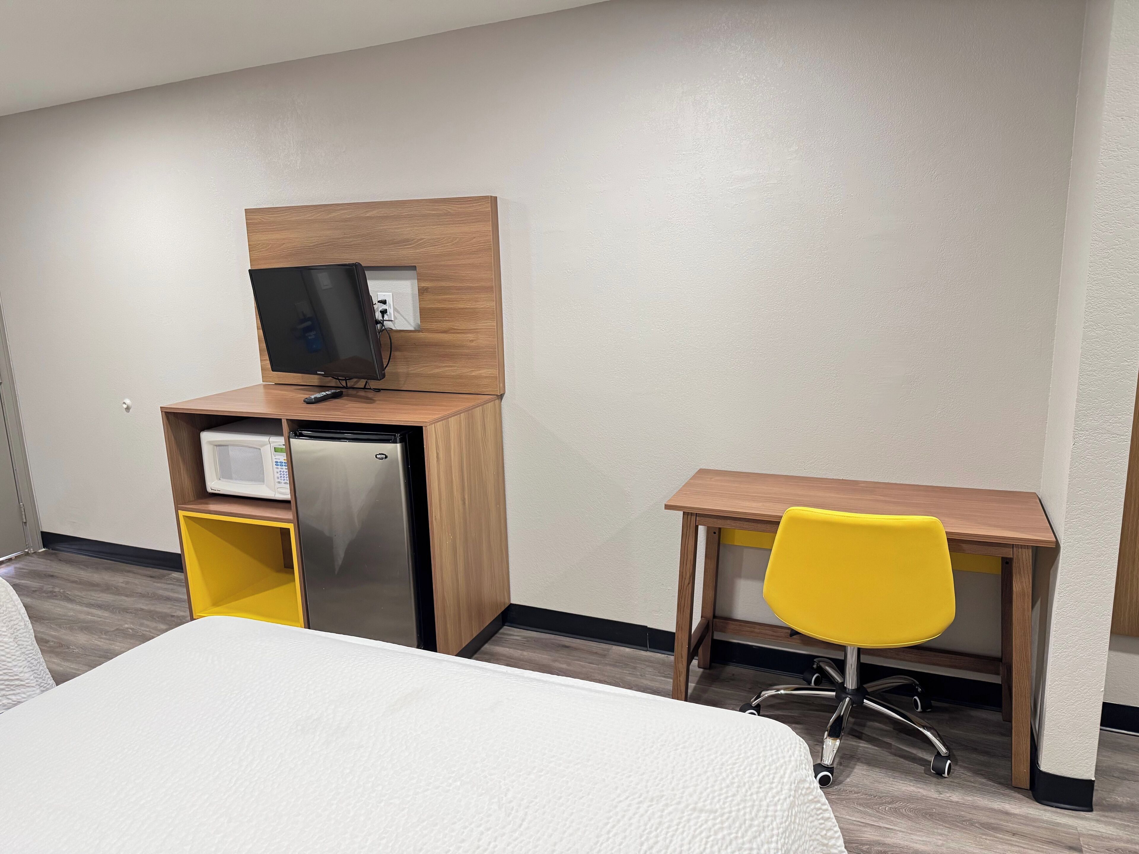 Quarto de hotel com uma cama, uma escrivaninha com cadeira, televisão e frigorífico.