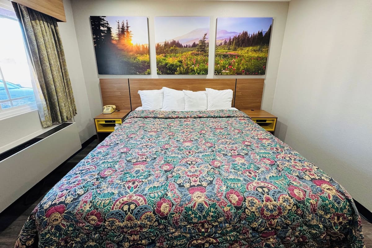 A hotel room with a large bed, a wooden headboard, two bedside tables, and a window with curtains.
