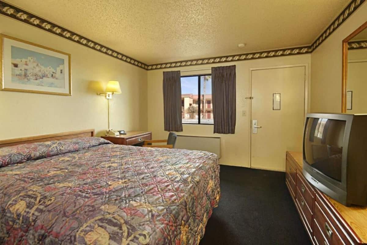 A hotel room with a bed, a desk, a chair, a television, and a window with curtains.