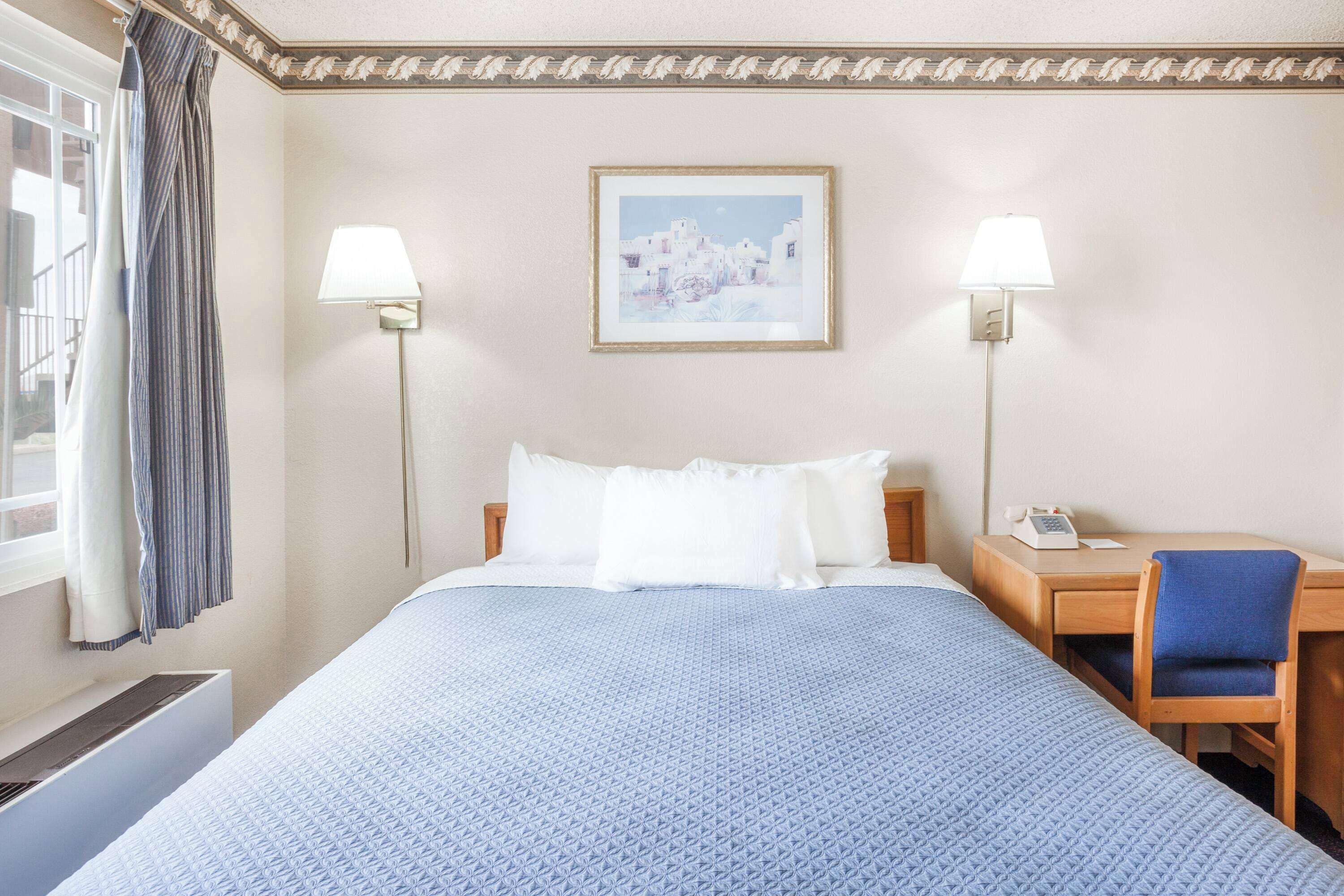 A hotel room with a large bed, two bedside lamps, a desk with a chair, and a framed picture on the wall.