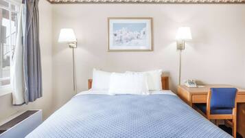 A hotel room with a large bed, two bedside lamps, a desk with a chair, and a framed picture on the wall.