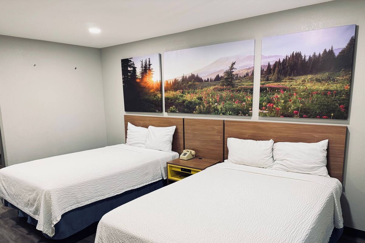 A hotel room with two beds, a wooden headboard, and a nightstand with a phone.