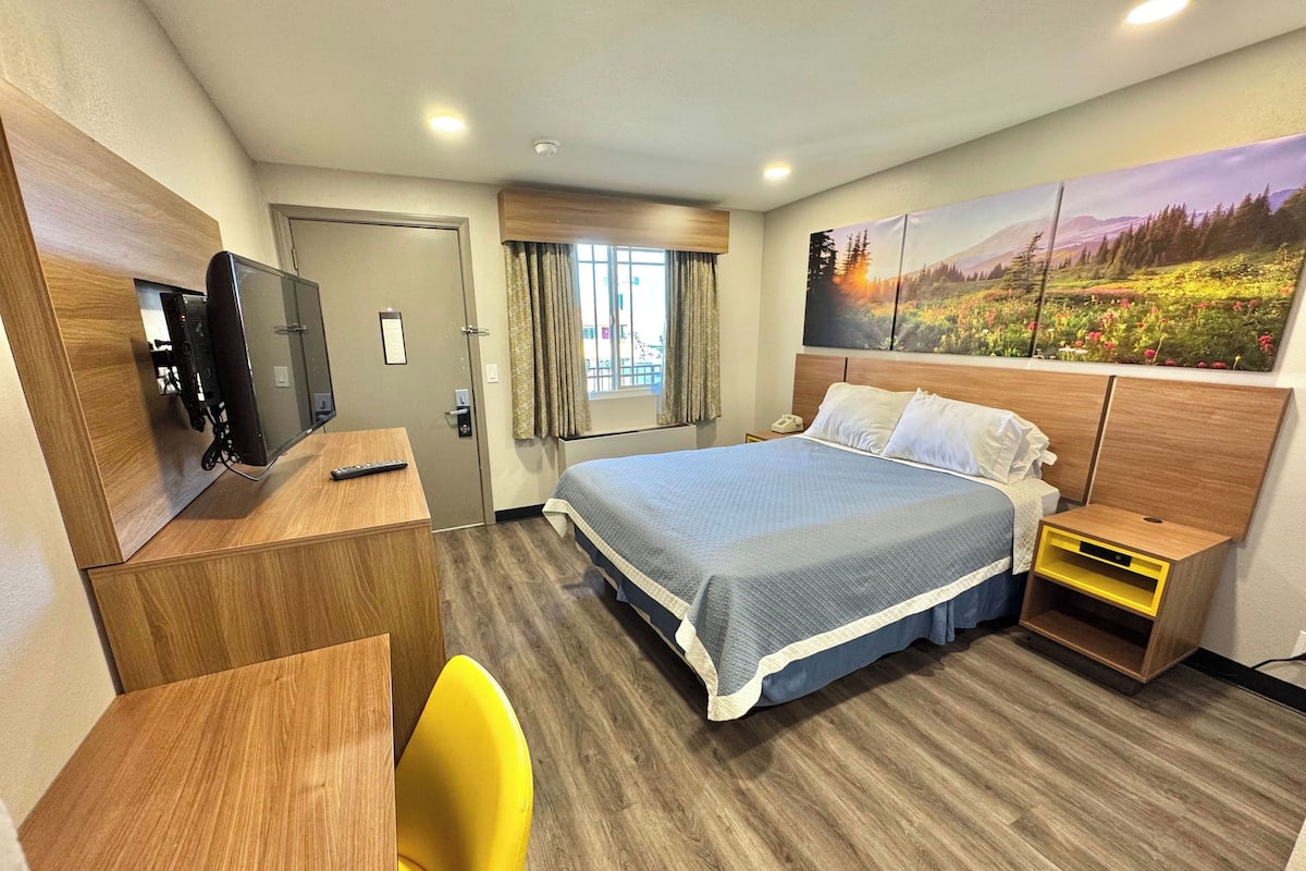 A hotel room with a bed, a desk, a chair, a television, and a painting on the wall.