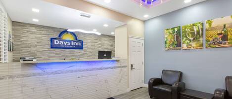 A reception area with a marble counter, a reception desk, and a sign that reads "Days Inn by Wyndham". There are two leather armchairs and a door in the background.