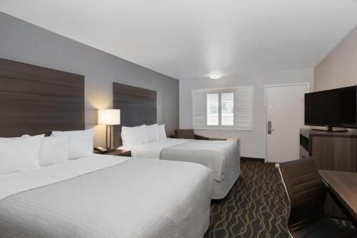 A hotel room with two beds, a TV, a desk, and a window.