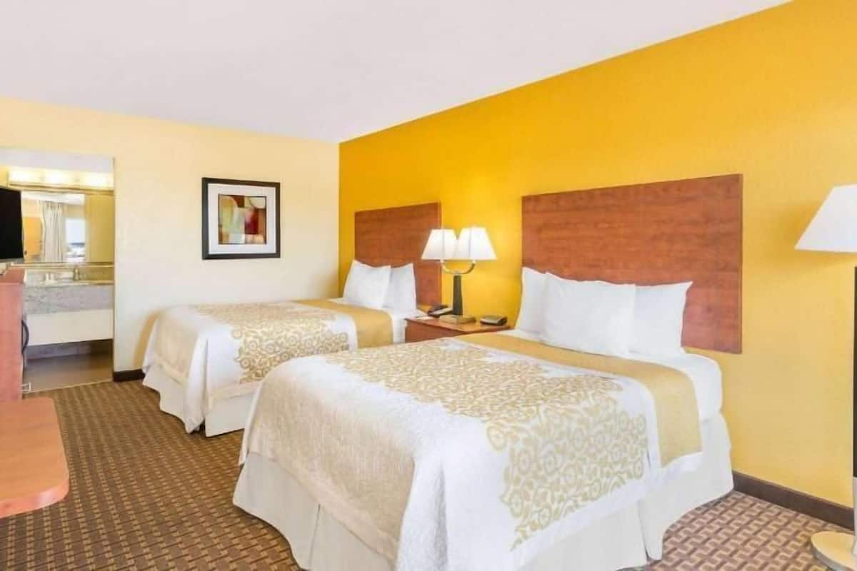 A hotel room with two beds, a desk, a chair, a TV, a lamp, and a framed picture on the wall.