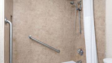 A bathroom with beige tiles, a white bathtub, a shower with a handheld showerhead, and a grab bar.