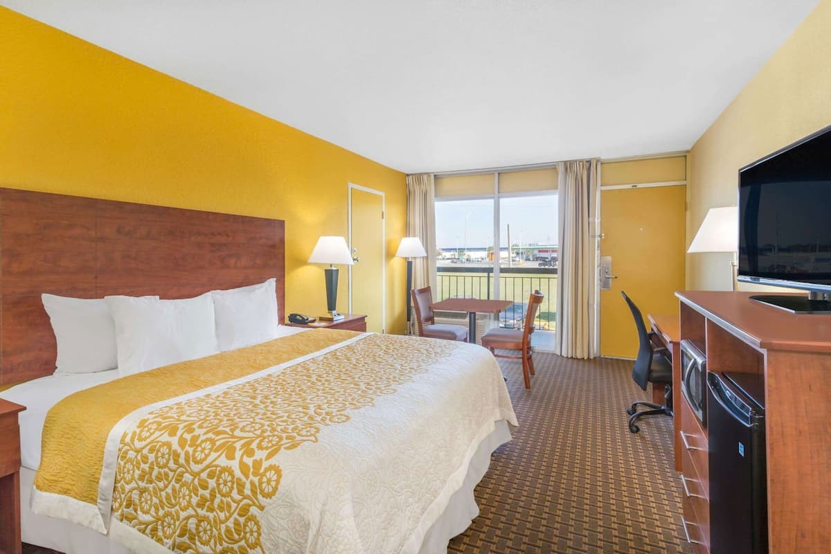 A hotel room with a large bed, a desk with a TV, a chair, a table, and a balcony with a view.