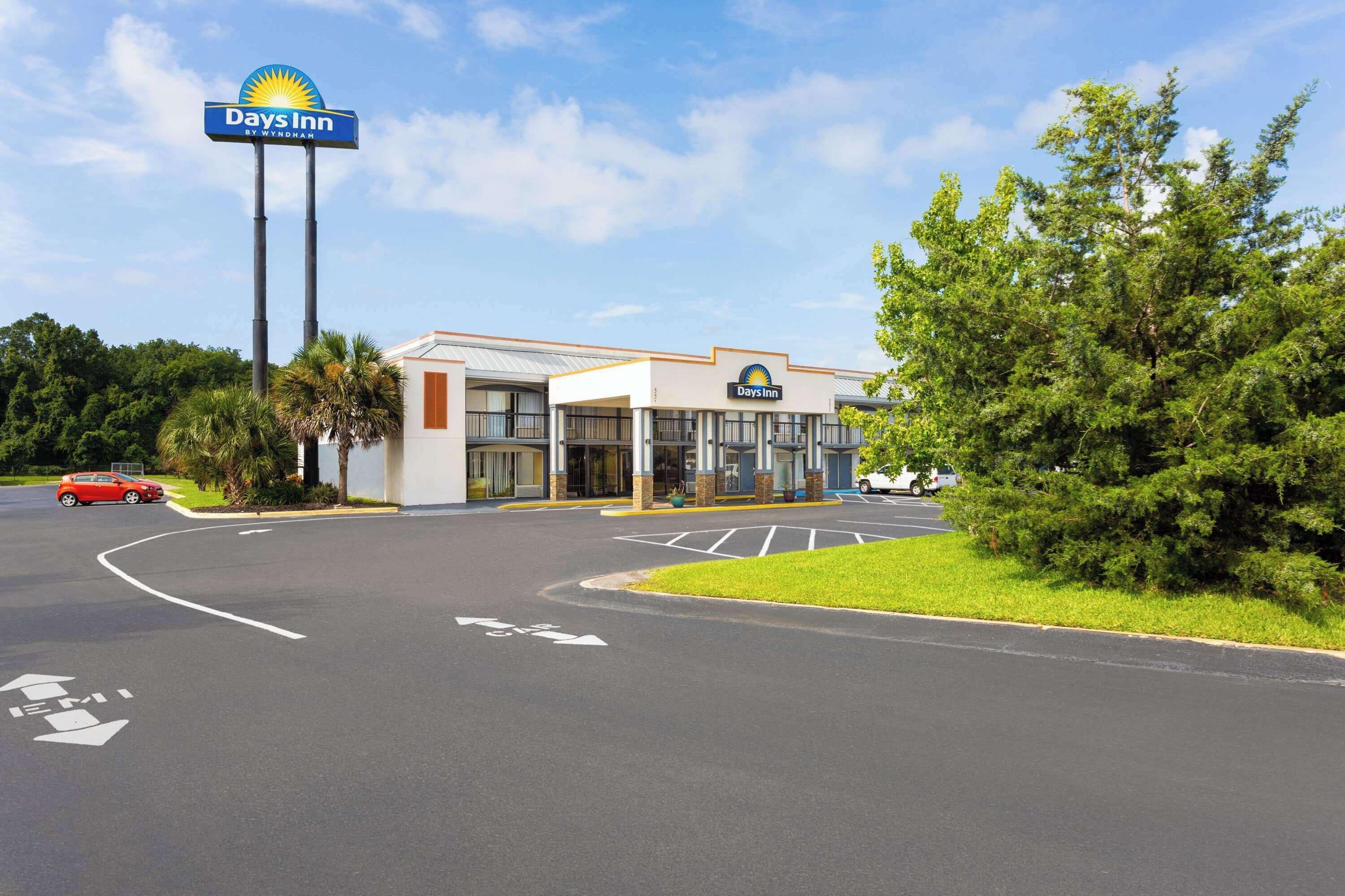 A Days Inn by Wyndham with a parking lot, a clear sky, and greenery around.