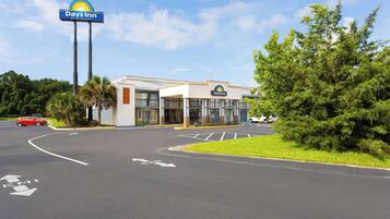 A Days Inn by Wyndham with a parking lot, a clear sky, and greenery around.
