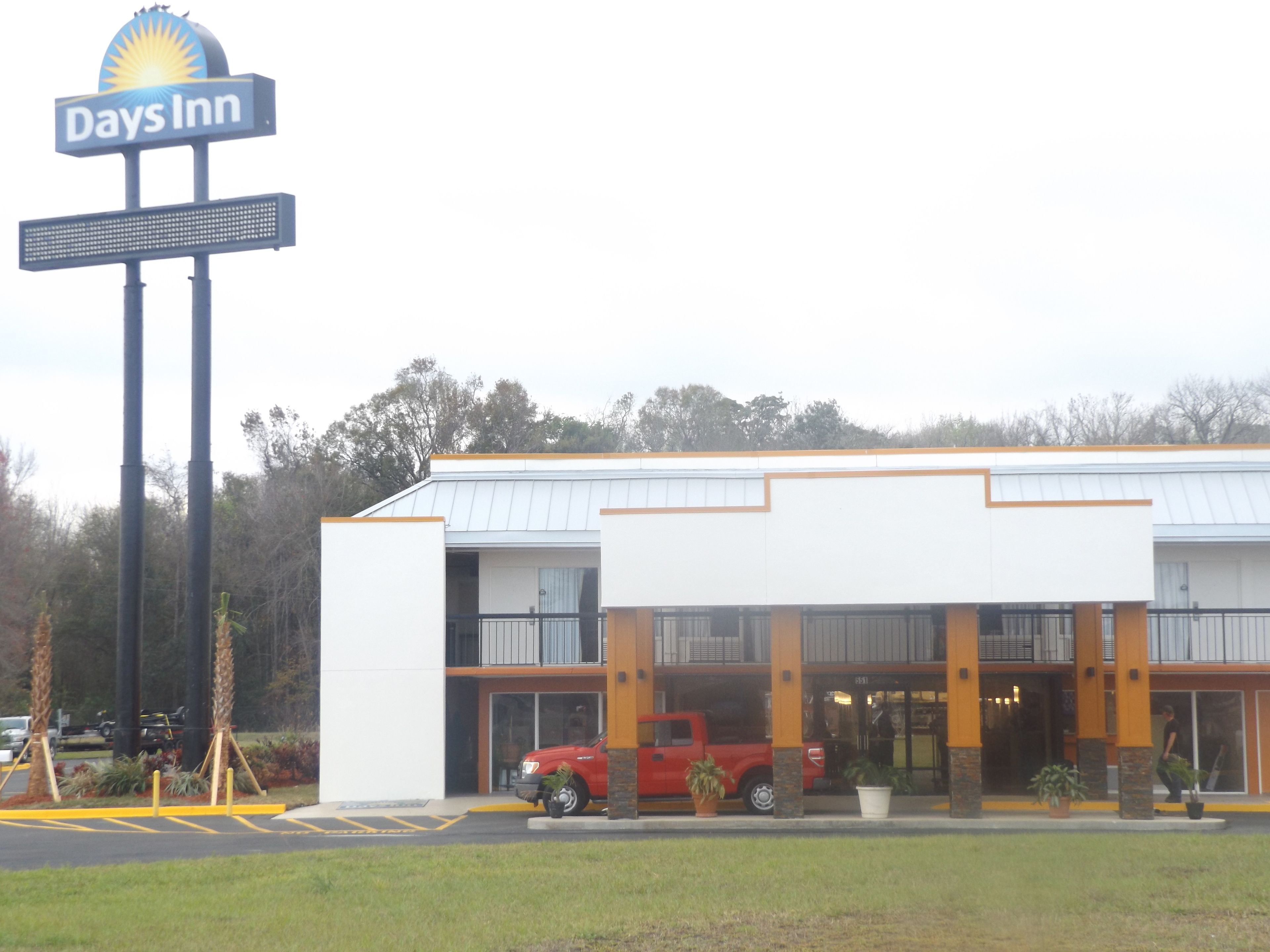 Un hotel Days Inn con un diseño moderno, que presenta una camioneta pickup roja estacionada frente, un gran letrero y un estacionamiento.