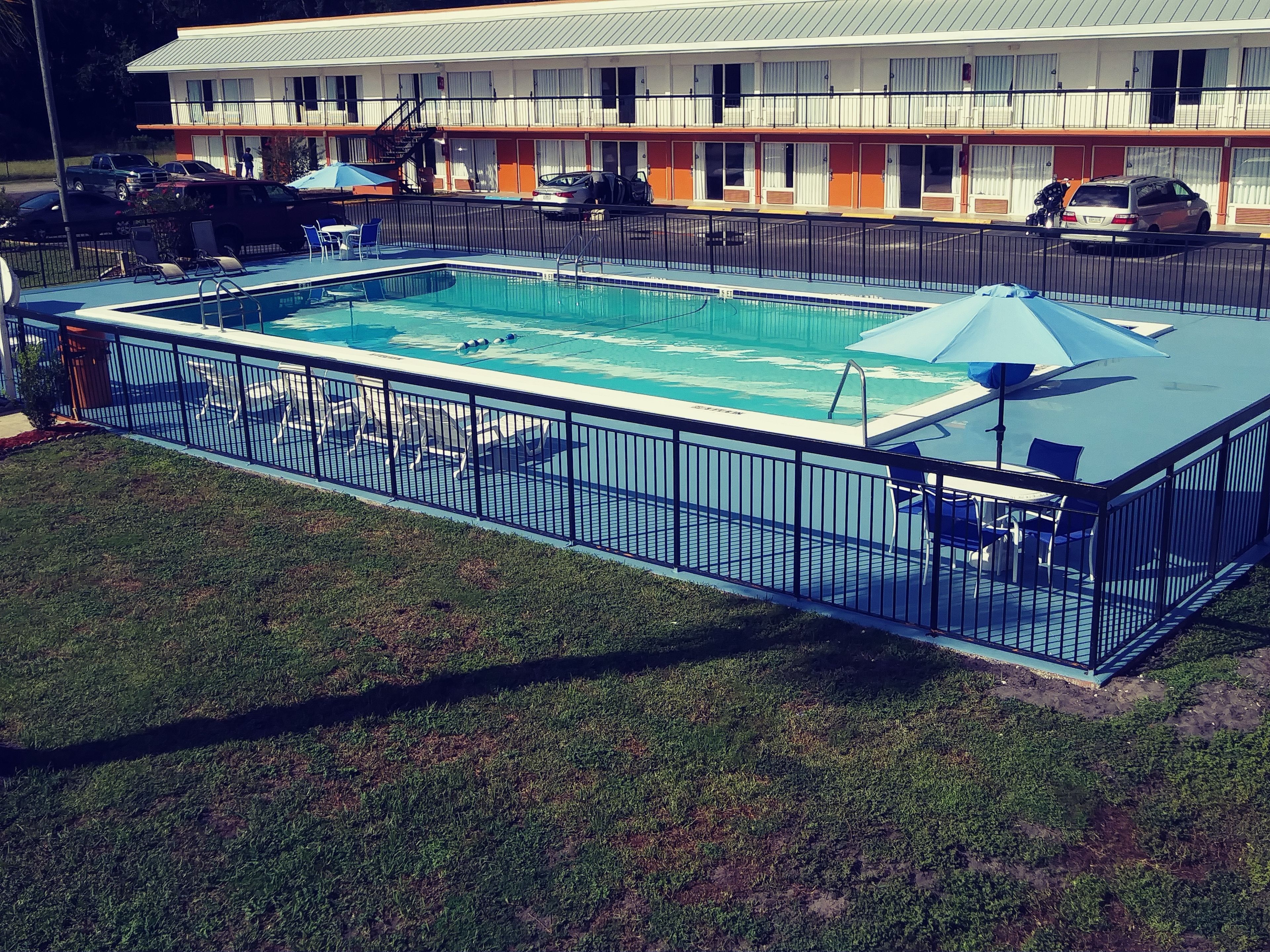 Une piscine rectangulaire dotée d’une terrasse entourée de clôtures, le tout bordé de pelouse.